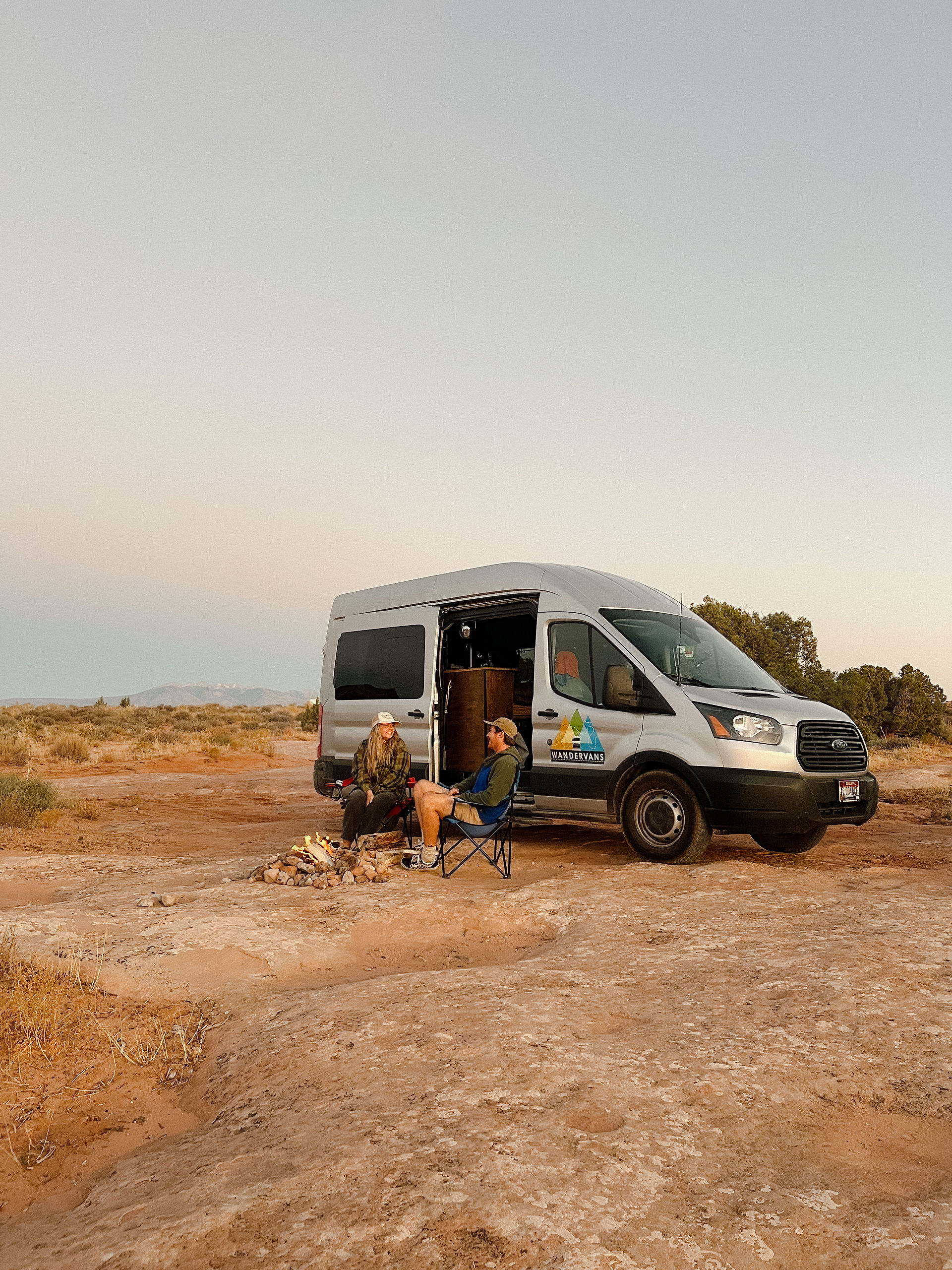 couple sitting around a campfire in front of a van