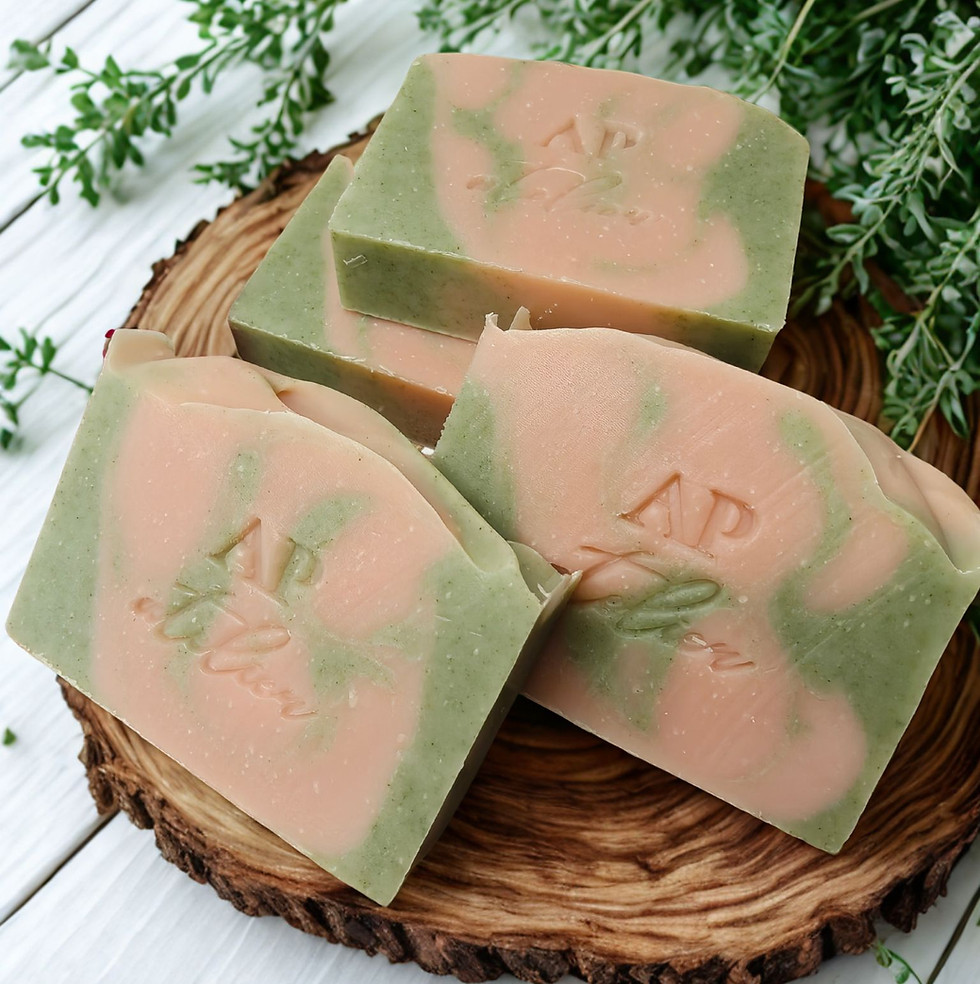 Handmade AP atelier natural soap bars with green and pink swirl design, displayed on a wooden slice with fresh herbs