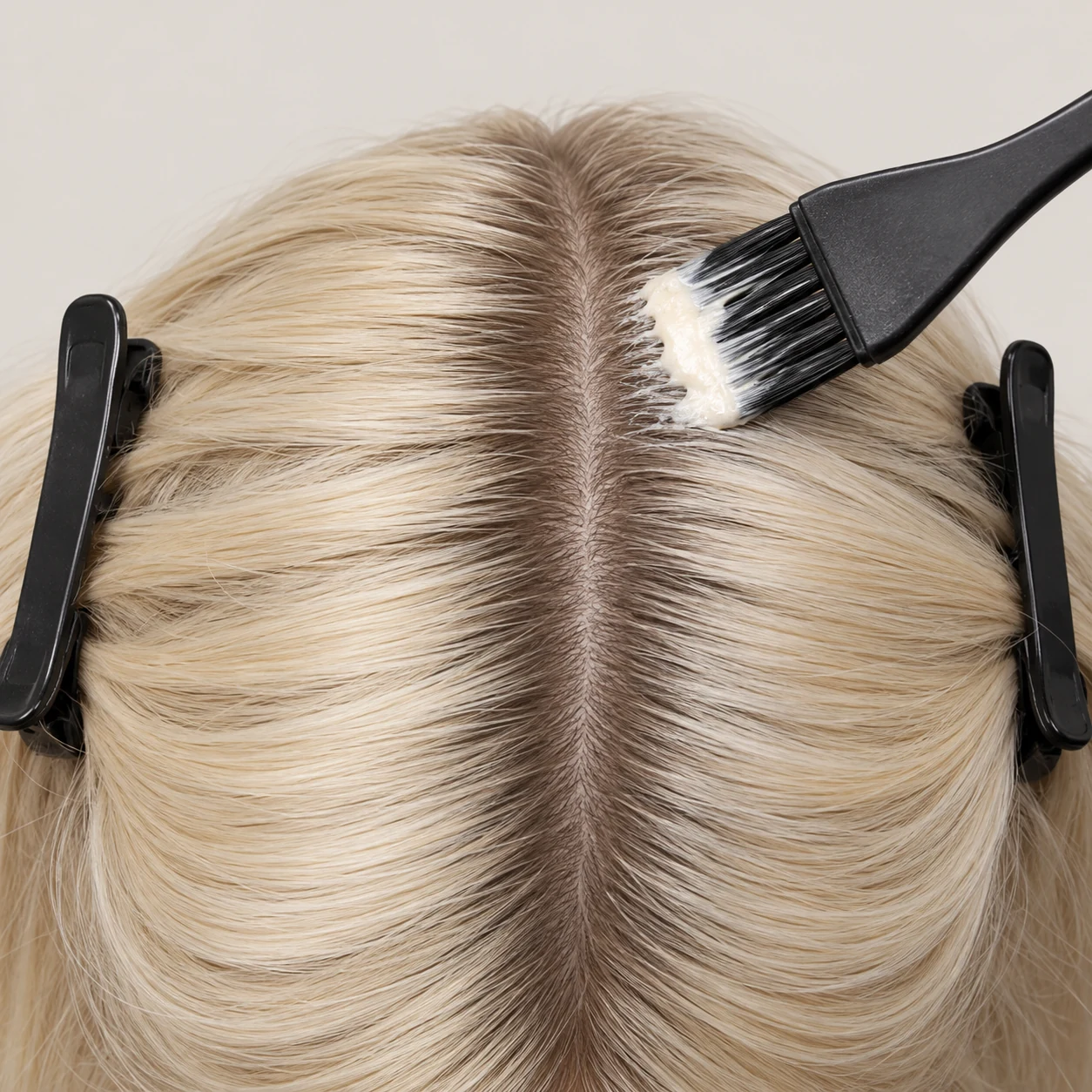 A narrow band of natural regrowth at the parting of sectioned blonde hair.