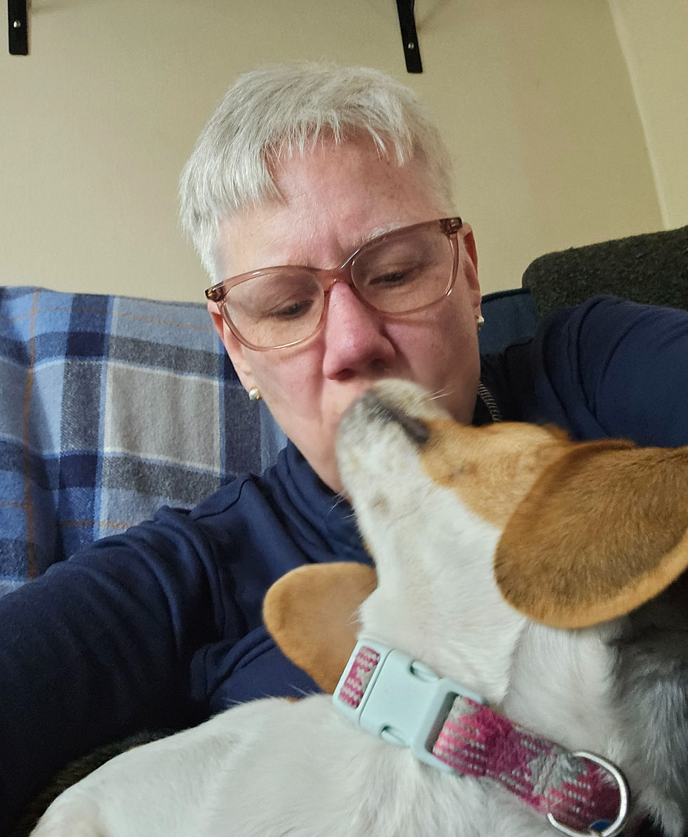 Woman with short white hair and glasses cuddles a small beagle dog in a blue plaid room, sharing a close kiss.