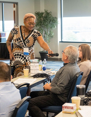 Lachandra B. Baker, founder of LBB Edutainment, conducts an interactive leadership training workshop, passing a microphone to a participant during a corporate speaking event.