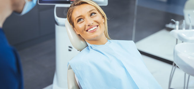 European young woman sitting in medical chair while dentist fixing her teeth at dental cli