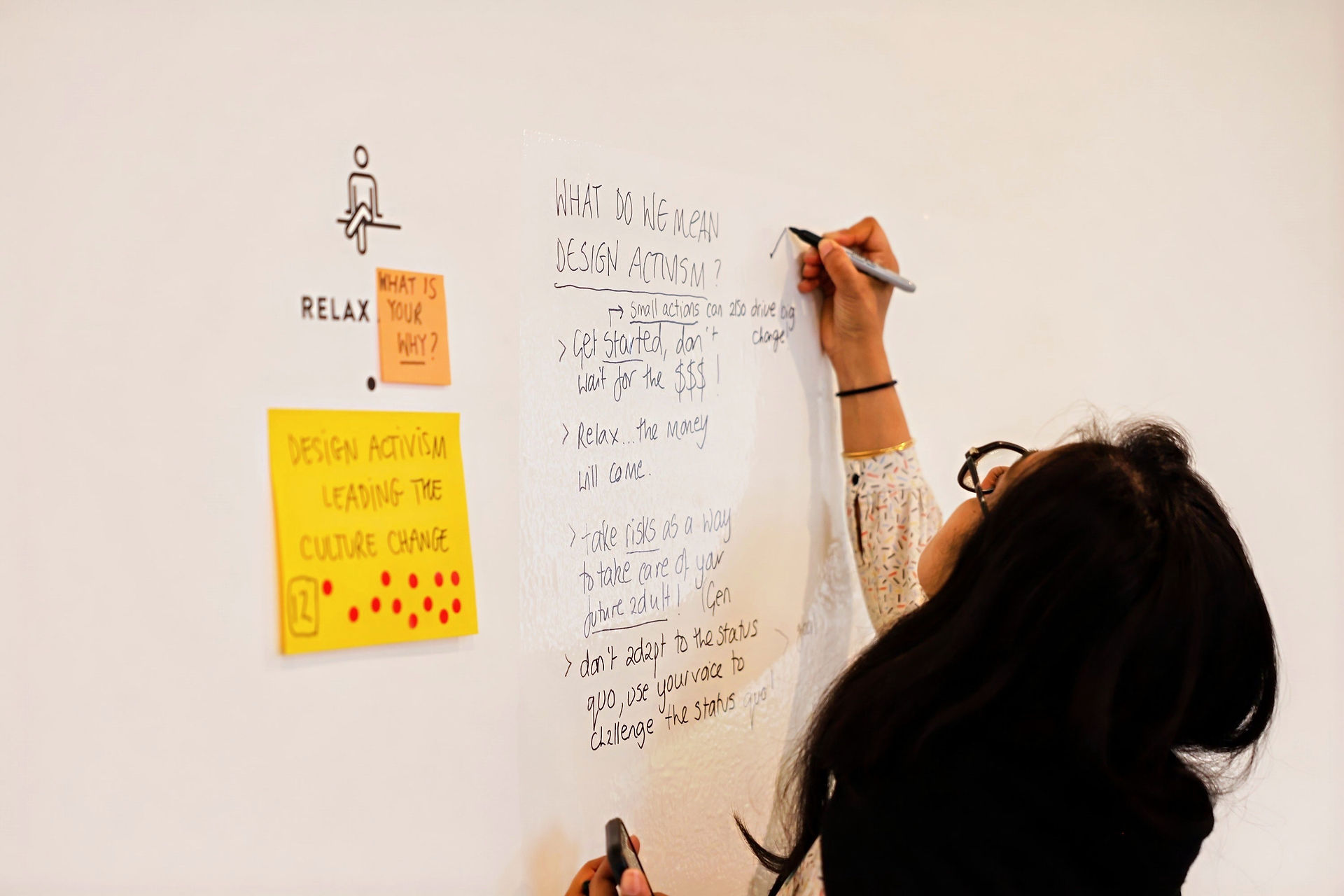 A person writing on a whiteboard with notes about design activism and two sticky notes