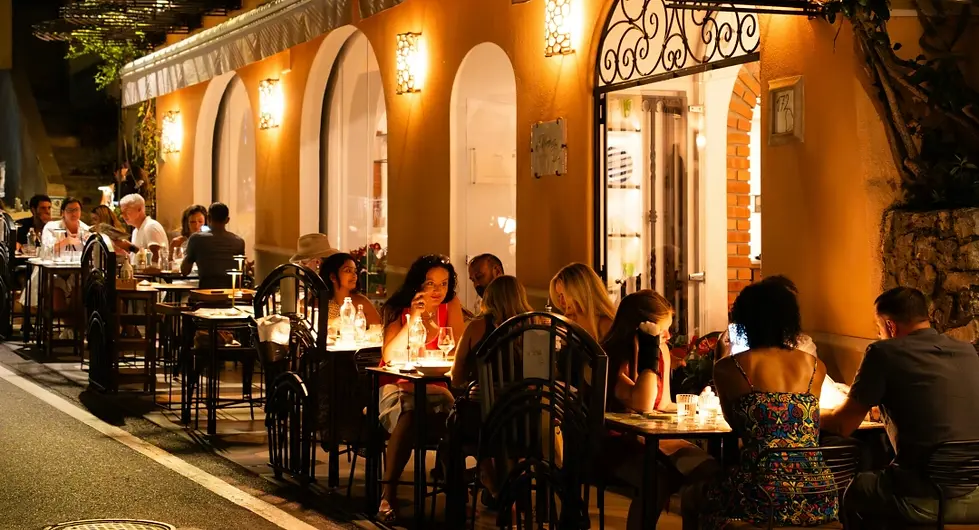 Terrasse de restaurant animée en soirée avec clients attablés sous des lumières chaudes – déploiement du concept hospitalité et expérience client en restauration – Patrimonio Hospitality