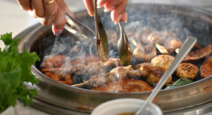 Live tabletop barbecue grill with marinated meats, seafood, vegetables, and skewers being cooked at the dining table for an i