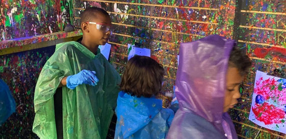 Children wearing ponchos and splattering canvases.