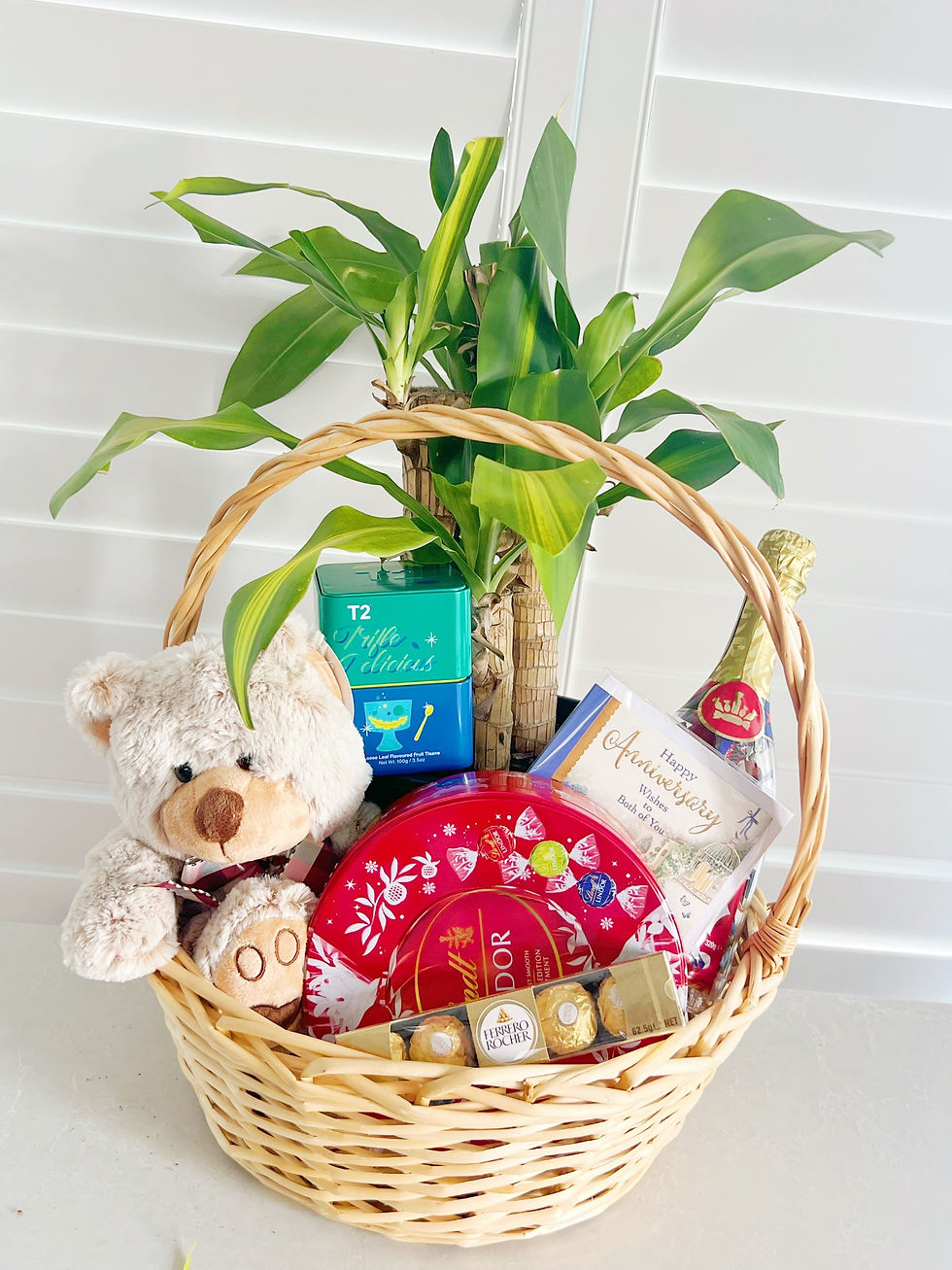 A gift basket including a teddy bear, champagne, chocolate and tea