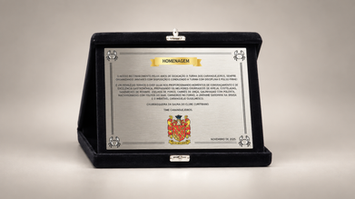 Placa de homenagem personalizada em estojo preto com brasão e texto institucional.