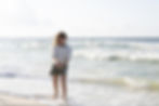 a young girl standing in shallow water holding a handful of wet sand containing mole crabs