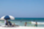 a set of beach chairs in the foreground as kids play in the Gulf water with June grass in the water too