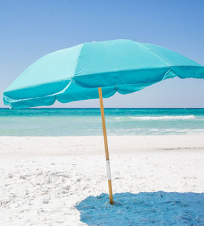 An aqua colored umbrella, open and planted on the beach behind Blue Mountain Beach Condos