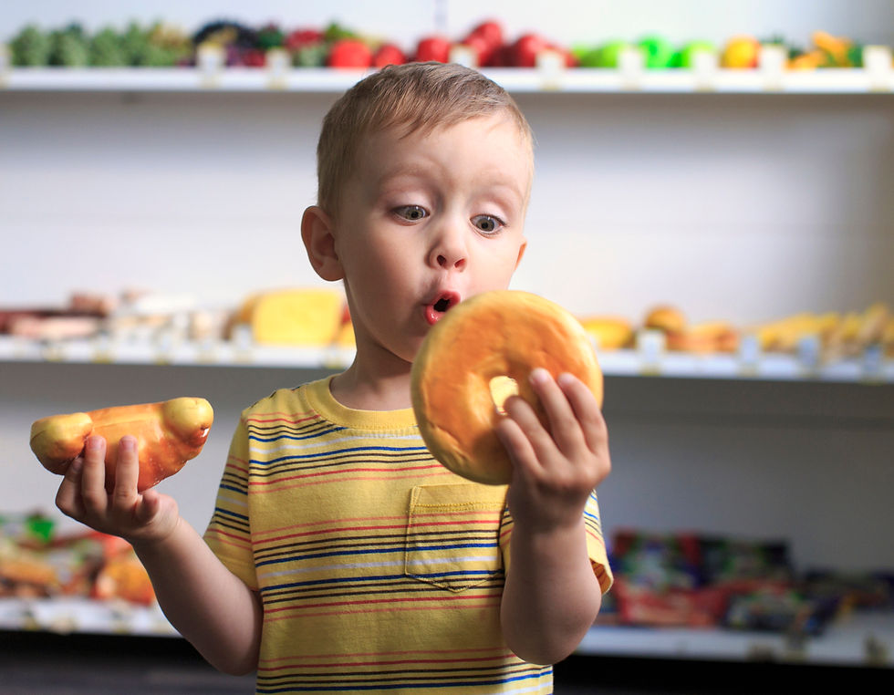 Toddler is excited holding a bagel and a croissant. There are shelves of fresh food behind him. Toddler, snacks, food, fresh, excited, picky-eater.