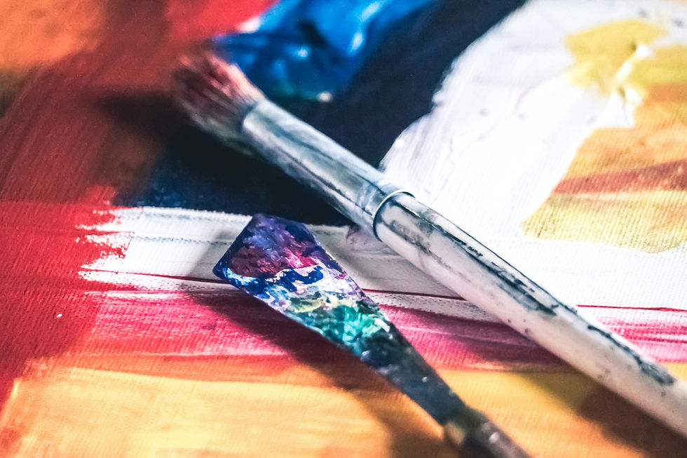 Close-up of a colorful paintbrush and palette knife on a vibrant abstract painting with red, blue, and yellow hues, evoking creativity.