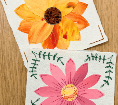 Two papers with embroidered flowers on a wooden desk background