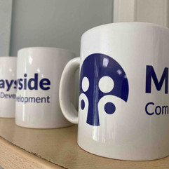 Shelf with three white mugs on it. Mugs have Murrayside Development Centre written on them, along with a logo