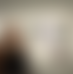 Woman in a black vest standing in front of three glass wall sculptures and various other decorative items on a shelf