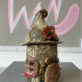 Handmade ceramic fairy house with a curved roof, small door, window, and red flower decoration.