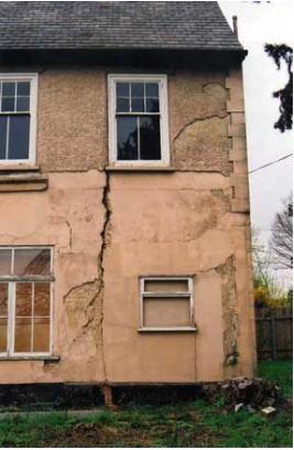 Image of the front corner of a large old house with cracks in the structure