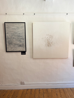 Two walls of an art gallery with five wall-mounted paintings