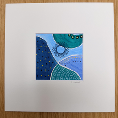 Fluid pattern piece of artwork in blue, green and white with gold embellishments and a stitched spiral-style star embroidered on it. The picture is in a white mount with a signature on it