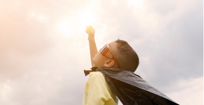 little boy with superhero cape raising arm to the sky