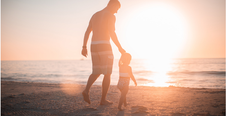 man and young boy holding hands on the beach at sunset