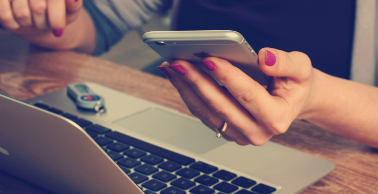 woman holding phone in one hand and typing on laptop with other