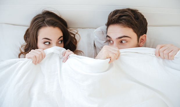 funny-young-couple-lying-and-hiding-under-the-blanket-in-bed-SBI-302840463.jpg