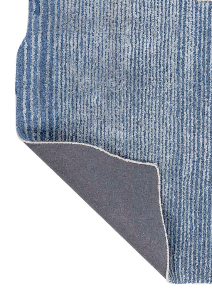 Thumbnail: Folded corner of a blue striped rug revealing grey fabric backing, light edge binding and textured vertical lines.