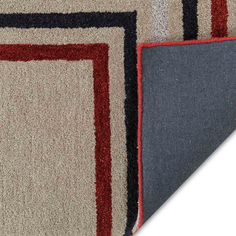 Thumbnail: Beige rug with red and navy angular lines and a folded corner revealing grey fabric backing and red edge binding.