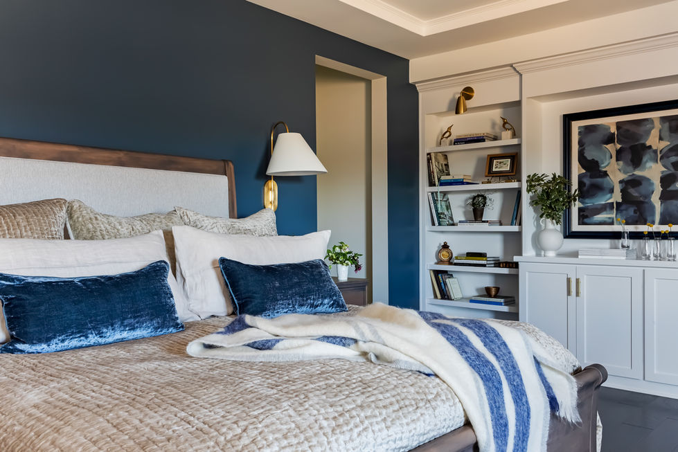 Deep blue walls and cream-colored comforter make the bed pop - with a white wall of built ins featuring personal memories and custom artwork