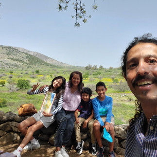 Sagi Levy with a family sitting on an ancient stone wall in a blooming green valley in Israel.
