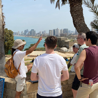 Sagi Levy private tour guide pointing from an Old Jaffa viewpoint to explain the history of the Tel Aviv coastline to a group of tourists.