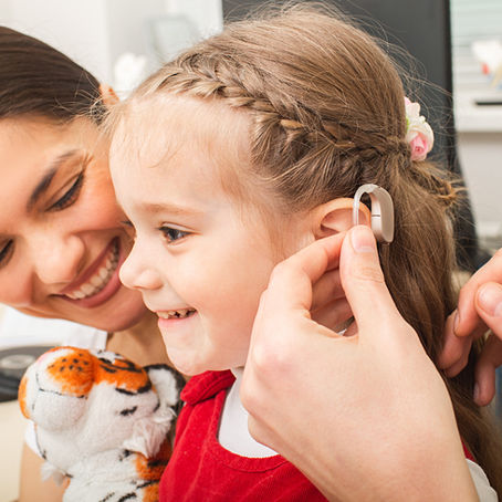 Smiling girl wearing a hearing aid with her mother — Topeka ENT provides tips to help children wear and care for their hearing aids.