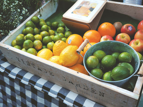 Crate of fresh fruit including oranges, limes, and green plums on a checkered surface.