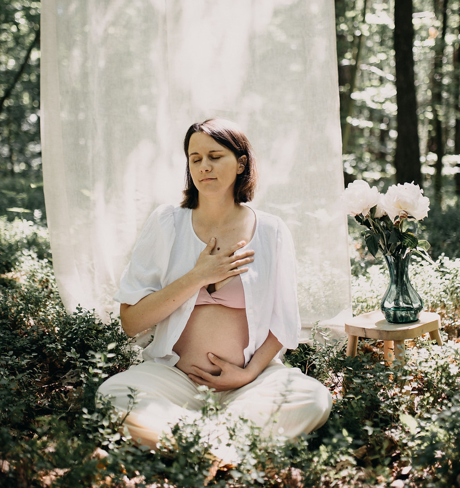 schwangere Frau, sitzend, meditierend und lächelnd, Augen geschlossen, eine Hand auf Bauch, eine Hand auf Brust
