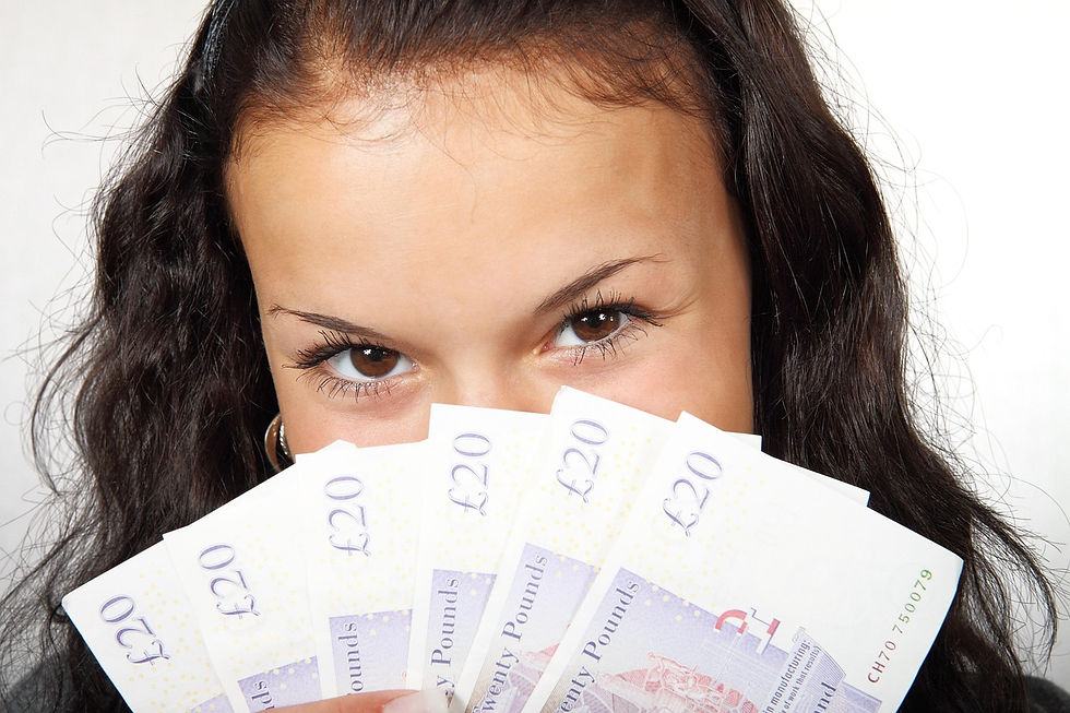 Woman with dark hair playfully holds up a fan of £20 notes, partially covering her face. Background is plain white.