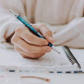 A female hand holding a pen and putting it to a paper journal to handwrite some text