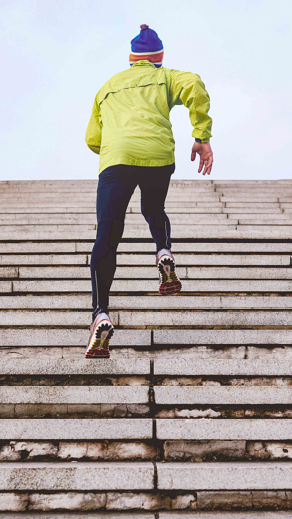 A man dressed warmly in athleisure runs up a set of outdoor stairs.