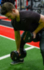 A man holds two 40lbs dumbbells, bends forward and lifts one at a time towards his chest during gorilla rows.