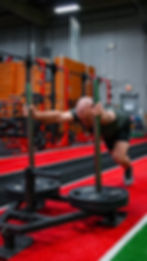 A man pushes a loaded sled on turf while inside a gym.