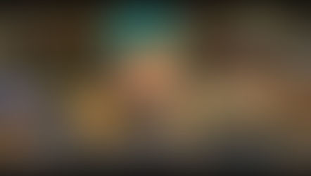 A character with teal hair and glasses in a rustic room. A table with papers and a sword is visible in the background.