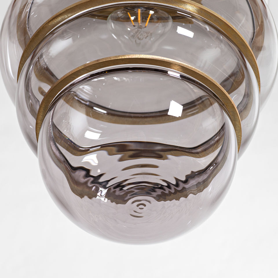 Close-up of glass pendant lamp by Stoft Studio showing brass rings and rippled glass surface, highlighting Scandinavian lighting craftsmanship.