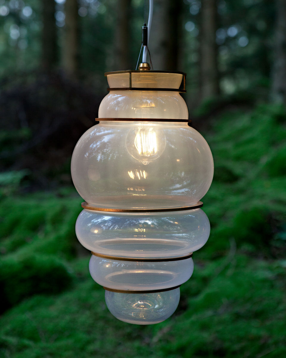 Elegant glass pendant lamps by Stoft Studio, designed with organic, beehive-inspired forms and warm golden fittings. Captured in a serene forest environment, this installation embodies the essence of Scandinavian lighting design — merging sustainability, craftsmanship, and poetic light expression. Ideal for architects, designers, and homeowners seeking nature-inspired, modern lighting solutions with timeless Nordic aesthetics.