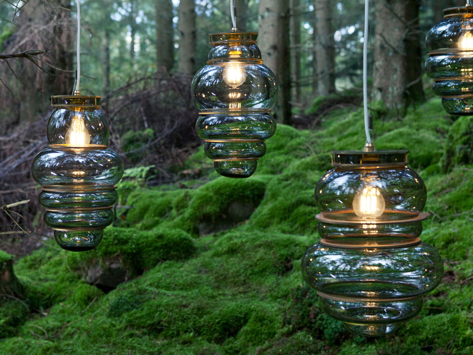 Handcrafted glass pendant lamp by Stoft Studio, featuring an organic, layered form in frosted glass with warm brass details. Suspended in a lush forest setting, the light embodies Scandinavian lighting design, blending craftsmanship, sustainability, and modern Nordic aesthetics. Ideal for searches related to Scandinavian lighting design, handcrafted pendant lamp, glass lighting, sustainable interior design, and modern Nordic craftsmanship.
