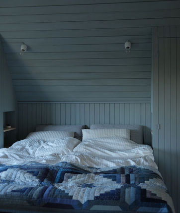 Cozy Scandinavian bedroom design by Stoft Studio with soft blue wood paneling, built-in storage, and a handmade quilt, blending minimalism with Nordic warmth and craftsmanship.