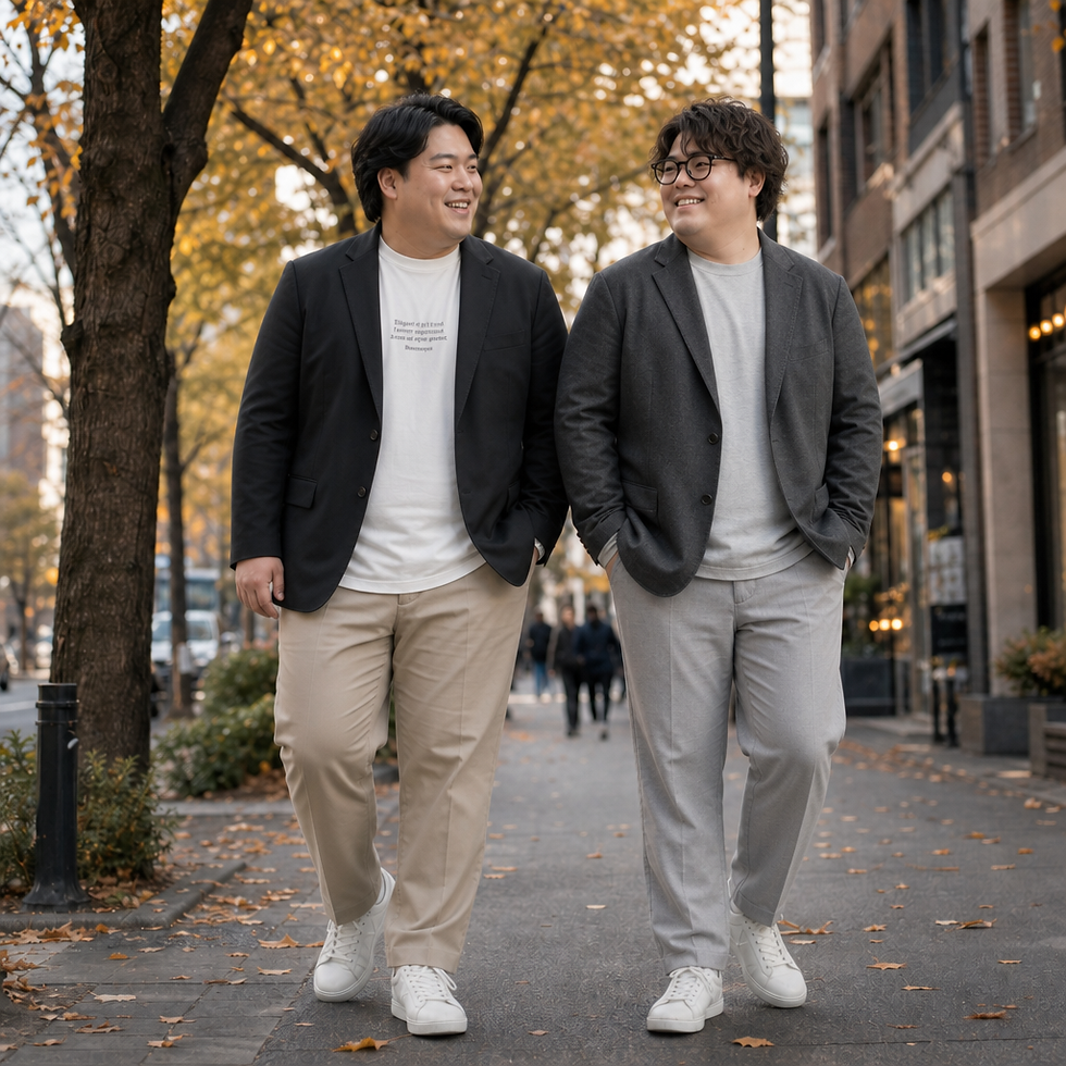 秋の街路樹の下、黒とグレーのジャケットに白いスニーカーを合わせた男性2人が笑顔で並んで歩く、落ち葉の歩道