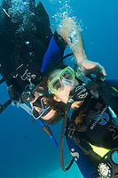 Instructor adjusting a returning diver’s tank height during a hover over sand.