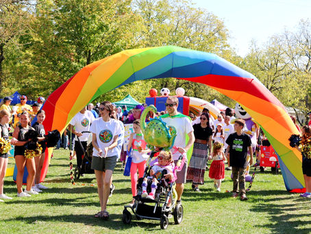 a family team walks and rolls under a rainbow arch cheered on by a crowd at lansdowne heroes walk and roll