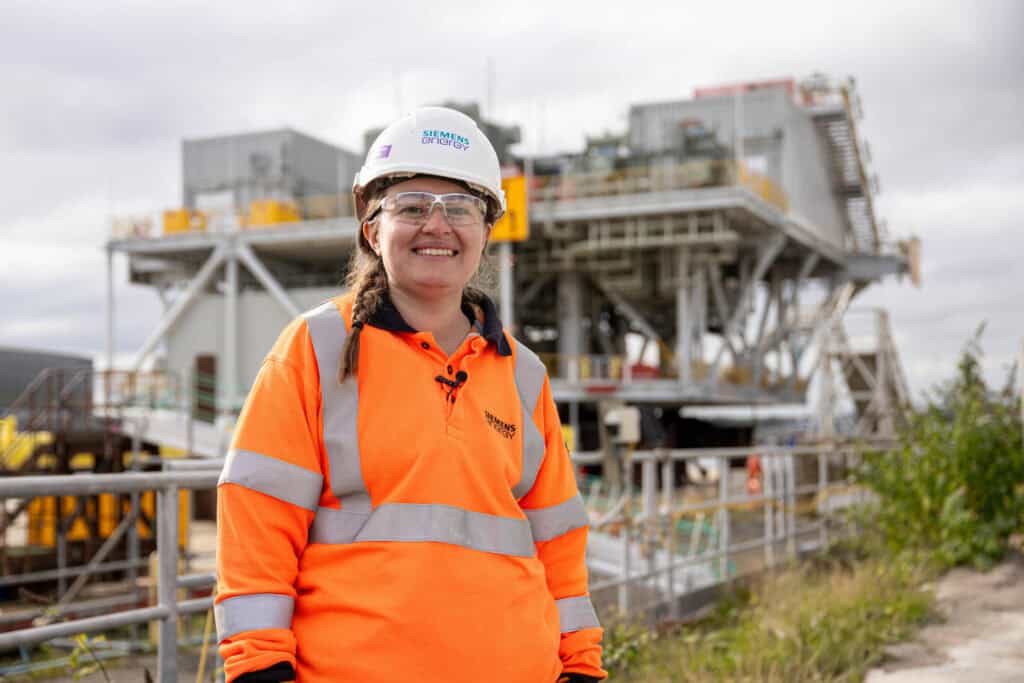 Siemans Energy Apprentice wearing hard-hat and high-vis jacket in front of manufacturing equipment